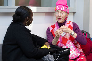 Two woman talk. One is wearing a black jacket the other is wearing a pink beanie and all pink/purple clothing