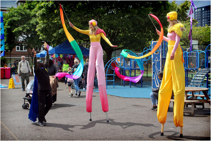 Slit walkers dressed in colourful outfits waving colourful ribbons at an outdoor festival