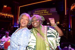 Two women grin together infront of a projected screen that reads