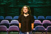 A young white woman in a black top smiling in front of theatre seats