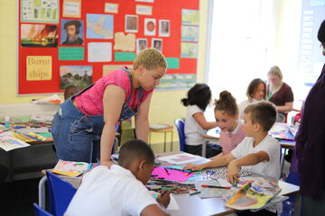 Woman leaning over table of children doing crafts 
