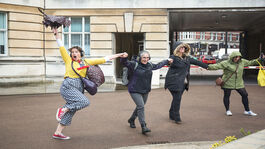 Four people in a line, holding hands and looking joyful. Some are skipping