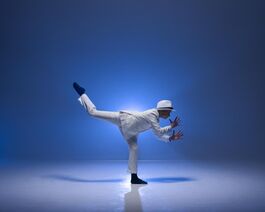 Young Dancer in a white suit with black ballet shoes in an attuite position looking like he is playing a jazz instrument