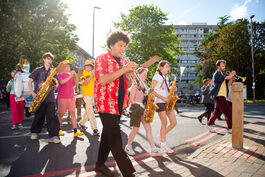 Group of people playing instruments, walking across a street, the sun shining