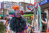 A person in a purple an dorange masks and feathered ruff poses with a plastic trident outside Tooting Broadway Station
