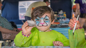 A boy with cat face paint holding up a rock he is about to paint