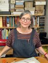 Woman in dungarees standing at desk in front of bookshelf