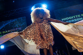 drag queen with afro in gold dress looking down at camera