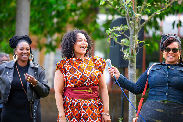 three women stand in a park laughing. The one in the middle wears clothes from the fashion designer fee uhssi.