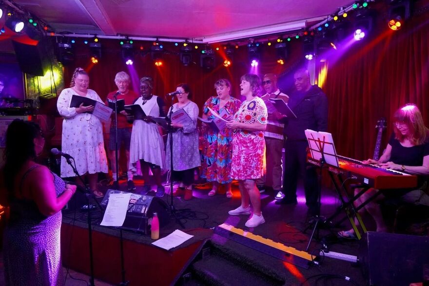 A group of people singing together under purple lighting 
