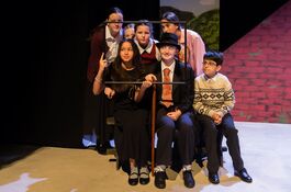 six young people sit in the middle of a stage and look through an empty photo frame