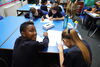 Boy turning to smile at the camera on a table of children, all writing