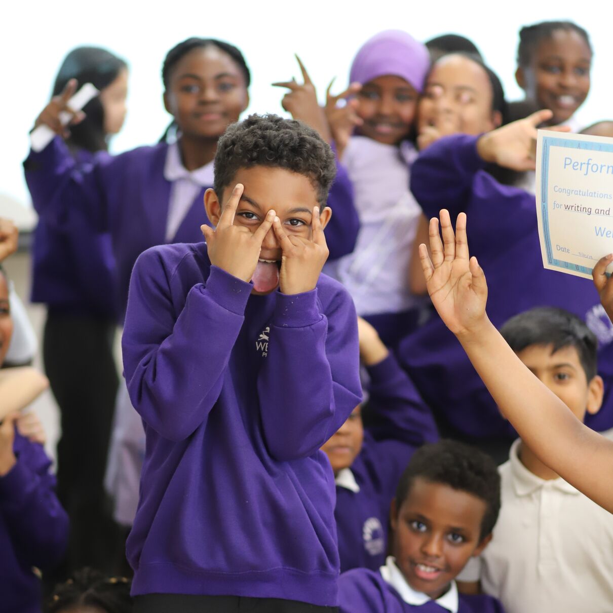 A boy surrounded by group of other school children pose for the camera
