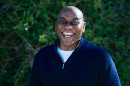 Ainsley Harriott laughing in front of hedge background