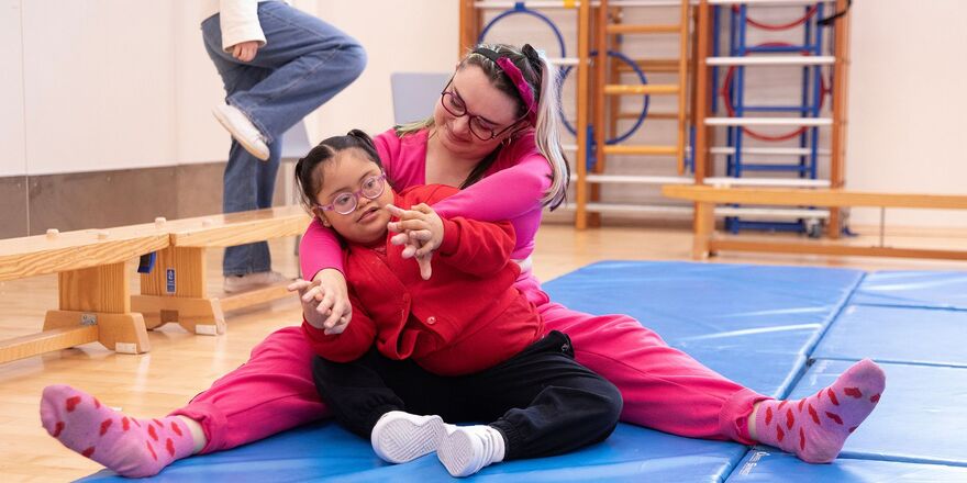 BLINK Co-Director Vicki, a white woman with bleached blonde hair, wearing a pink tracksuit, sits on the floor with a workshop participant.
