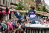 circus performers lock hands and lean over a crowd in the street