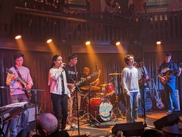 Group of young people on stage, singing and playing instruments, with spotlights 