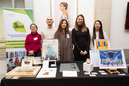 Five people stand together behind a table with their artwork on. Behind them is a pull-up banner with Re:Create on