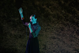 woman stands singing into a microphone with her arm in the air