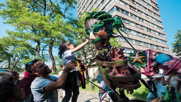 A dad holds his daughter up to touch a wooden festival scupture of a person