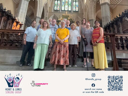 The friendly-looking and diverse members of Heart & Lungs Singing Group, standing, looking at the camera and ready to begin their singing session in their beautiful venue of All Saints Church, Tooting. 