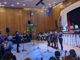 Small choir of children with a conductor performing in front of an audience.