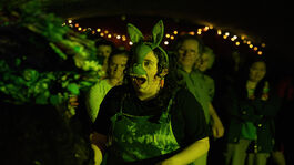 A person with a rabbit mask on looks surprised in dark green lighting