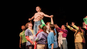 On a stage, one girl is being lifted by other cast members
