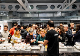 A group of people crowd around a counter in a commercial kitchen