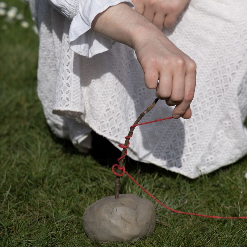 an artist sculpting outside with sticks / red string / clay