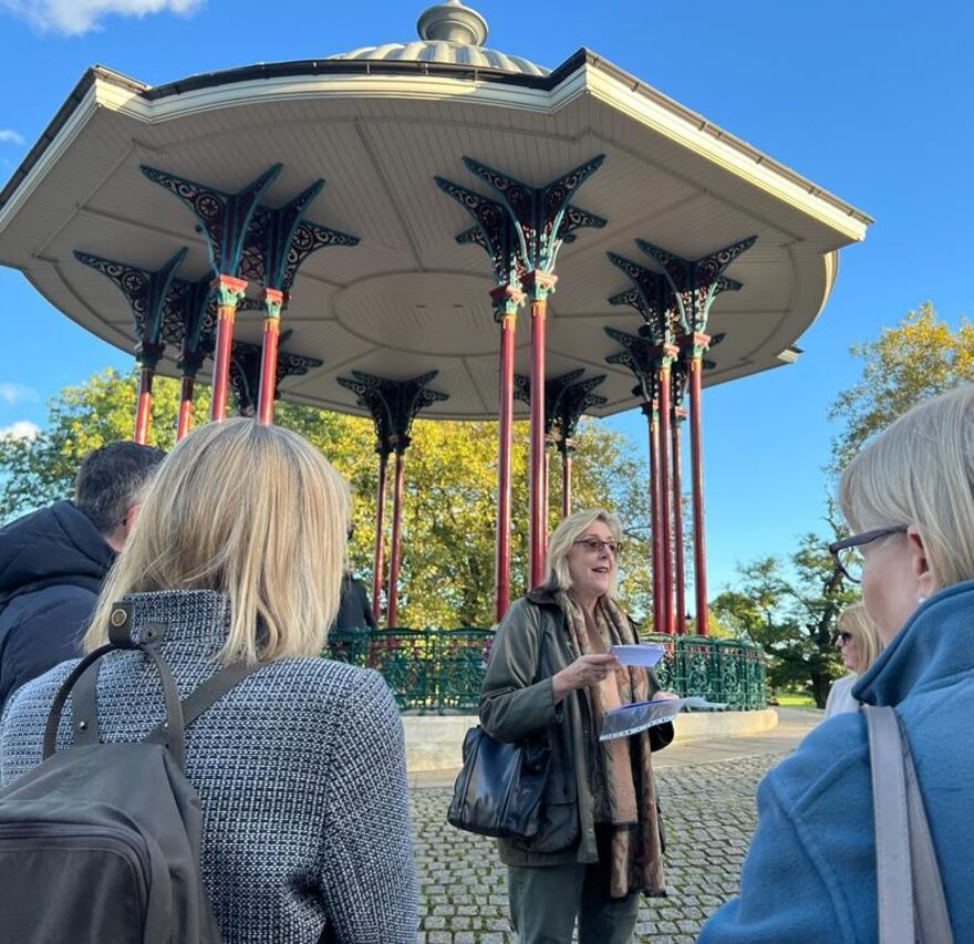 Group of walkers beside the Bandstand on Clapham Common with a guide.