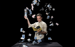 An image of a man reading a book whilst a confetti of playing cards falls around him.
