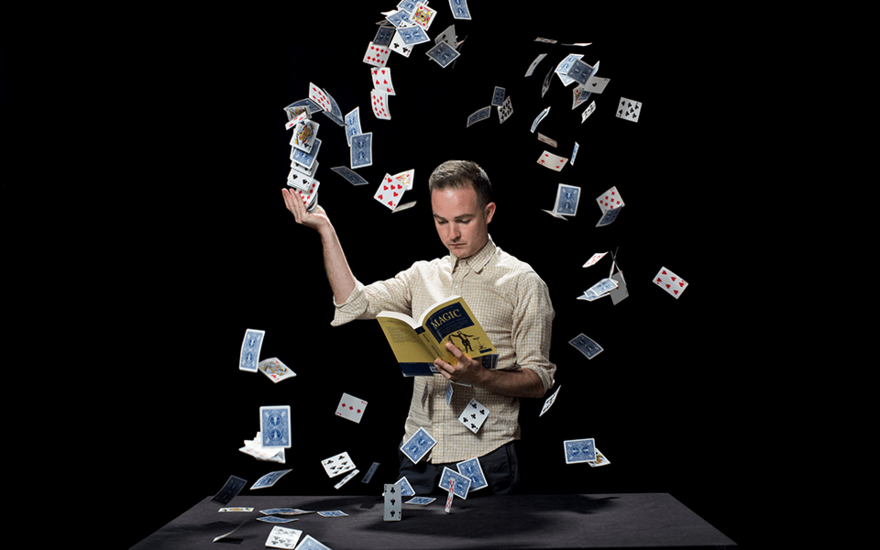 An image of a man reading a book whilst a confetti of playing cards falls around him.