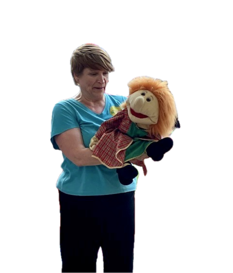 Woman standing up wearing a blue t-shirt and holding a child puppet with ginger hair.