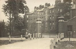Image shows the outside of Tooting Bec Asylum with a woman pushing a pram walking past.