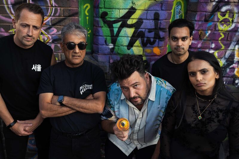 The band Moonshine Heavies pose in front of a wall with colourful graffiti