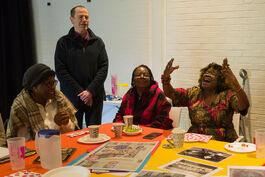 Three women and one man around a table and one of the women is singing