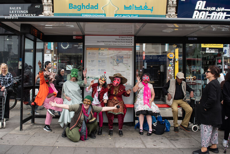Masked participants on a bus stop in The Church Street Masquerade 2024