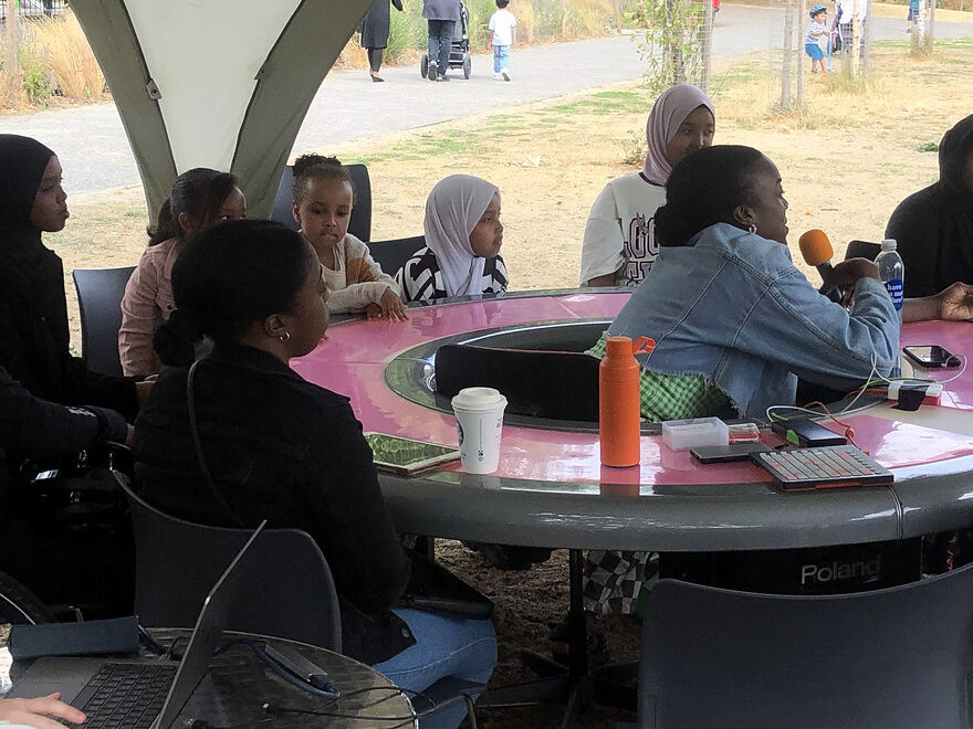 Groups of families sitting around a glowing pink table with a host in the middle holding a microphone