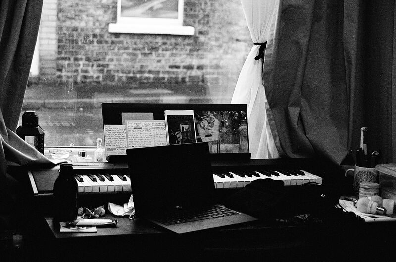 Black and white photo of desk with piano keyboard and laptop.