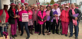 A group of singers wearing pink holding a sign saying Great Gustos. 