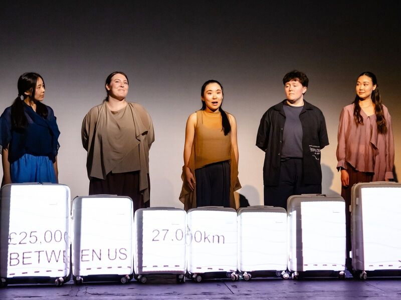 Production shots from Transit - the first is a group of actors crowded around a tower of suitcases while one pretends to take a selfie using a smaller suitcase; the second is a group of actors standing behind a row of suitcases with projections describing how much they've spent on migrating to the UK; the third is a group of actors clumped together in low light, their arms stretched out to the ceiling mid-contemporary dance; the fourth is an actor standing in between two harsh lights with words projected over her face; the fifth is five actors standing in the corners and centre of the stage, 'talking' to the home office via mimed phones.