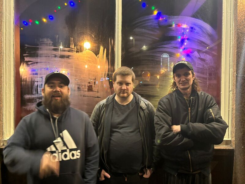 The Dub Righters wearing black standing by a window at night