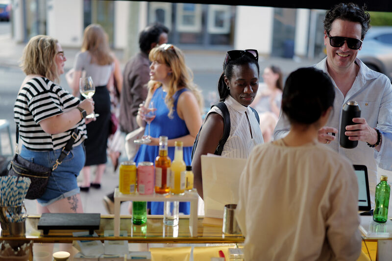 A ground of people, including two people facing each other having a conversation and laughing and two people ordering a drink at the till