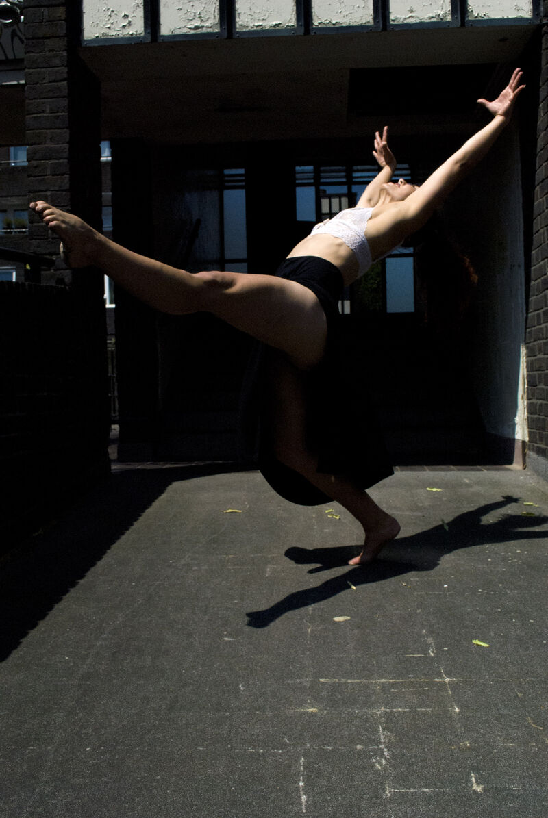 A woman dances, leaning back with her arms outstretched and one leg kicking up in front of her.