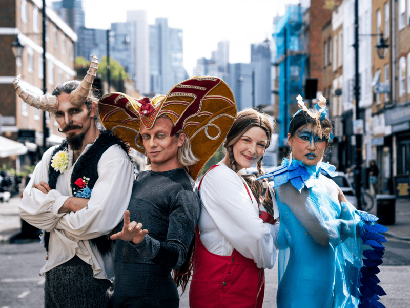 Four people in elaborate costumes standing in a city street, with buildings visible in the background