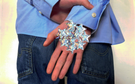 A hand is being held in front of a person wearing jeans and a blue shirt. Their palm is covered in silver stars. 