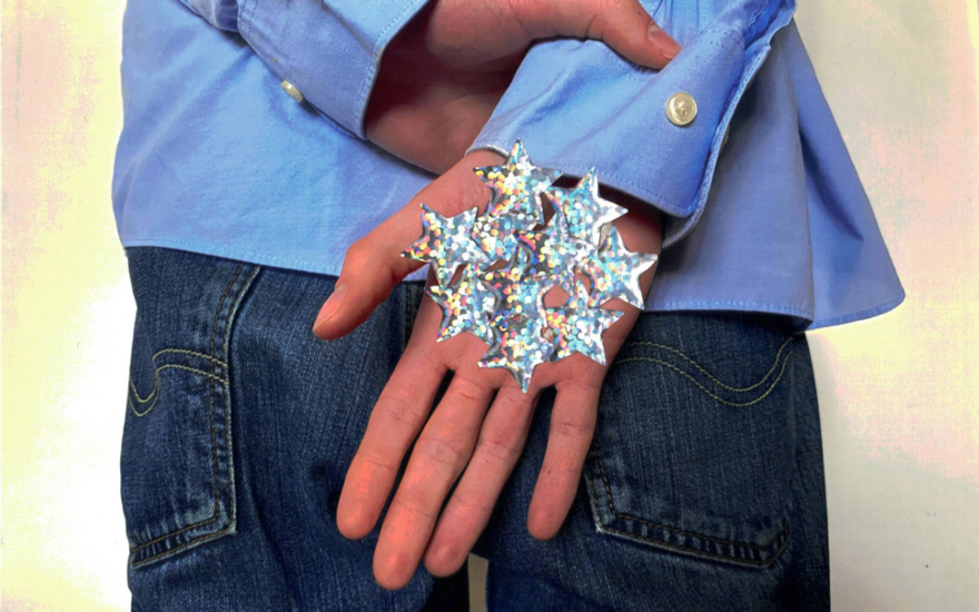 A hand is being held in front of a person wearing jeans and a blue shirt. Their palm is covered in silver stars. 