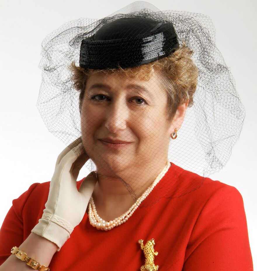 Performer in red dress, black hat with veil, necklace, earrings, broach, white gloves, hand to face
