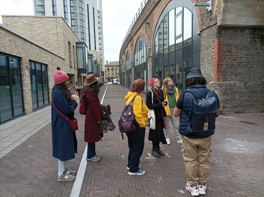 A group of people standing near a railway viaduct with a tall building in the background